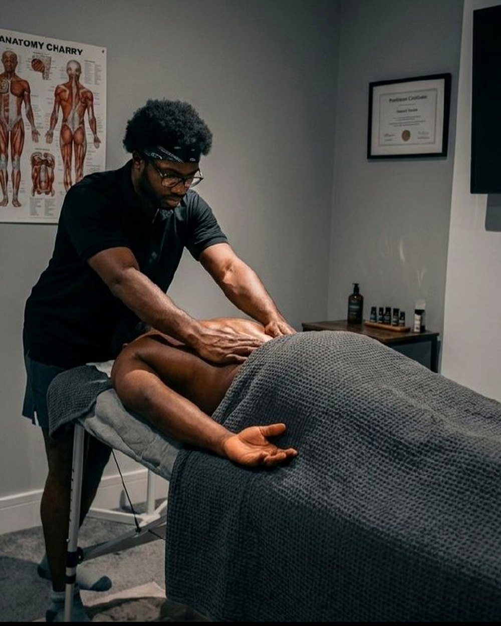 Focused back massage treatment with qualification and anatomy chart visible in the room.
